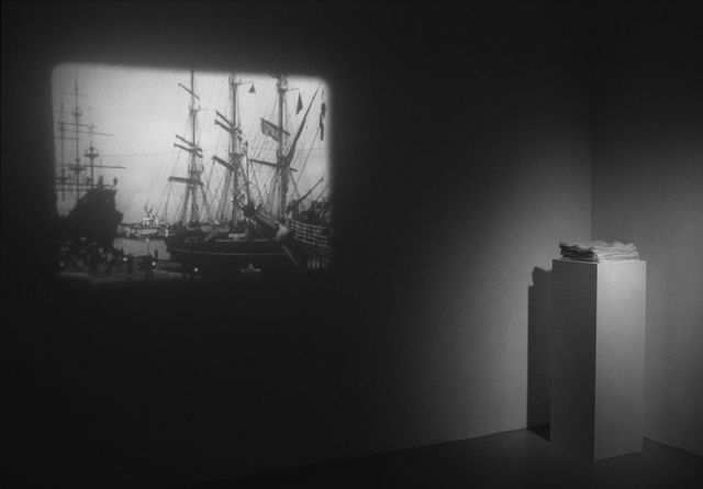 Amalia Pica, 16mm B/W film, 3 min 36 sec.  with stack of white handkerchiefs on white plinth, To Everyone That Waves (Installation view), 2005